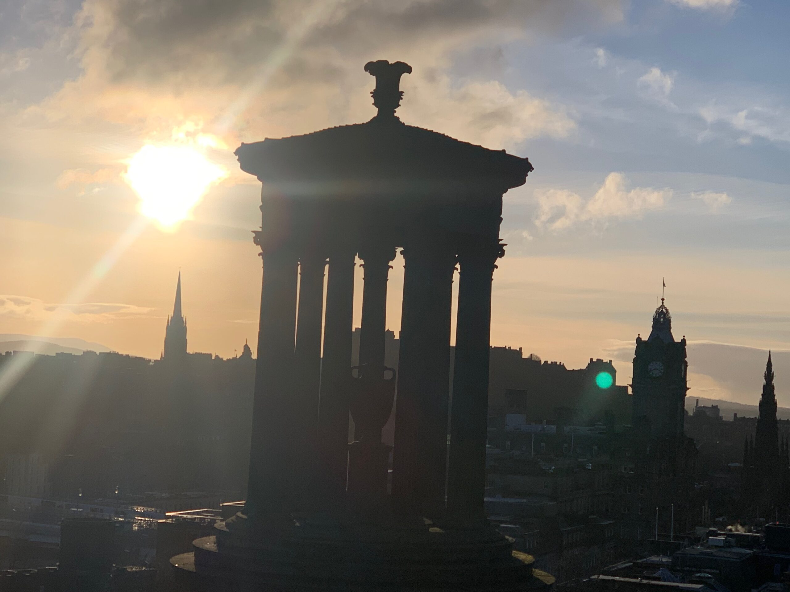 Dugald Stewart Monument on Calton Hill silhouetted at sunset over the Edinburgh skyline