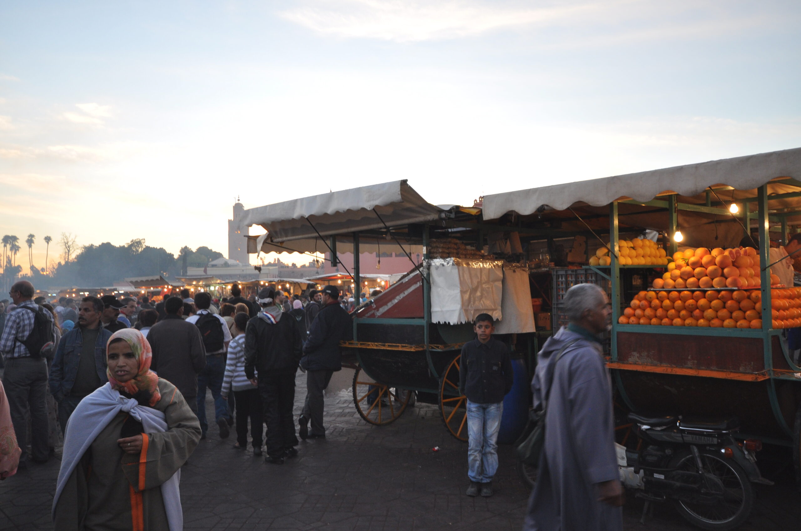Crowds and orange-juice carts fill Jemaa el-Fnaa square at dusk in Marrakech.
