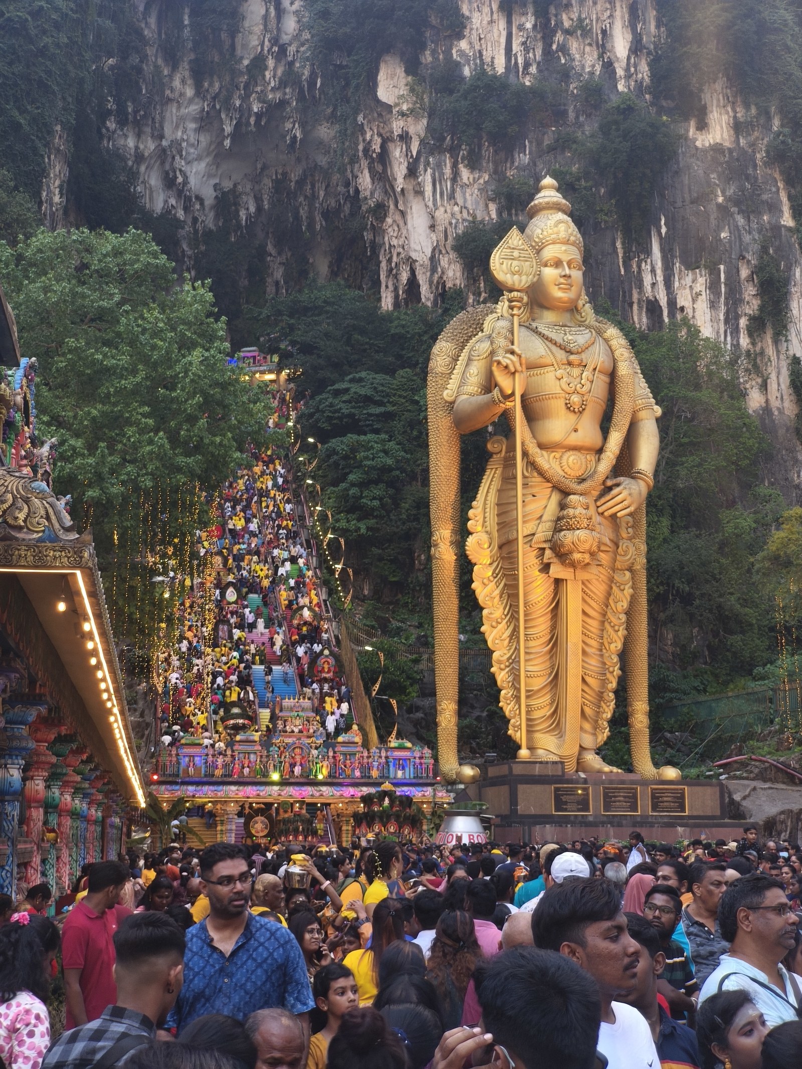 Golden Murugan statue and rainbow-painted stairs at the entrance to Batu Caves with devotees climbing