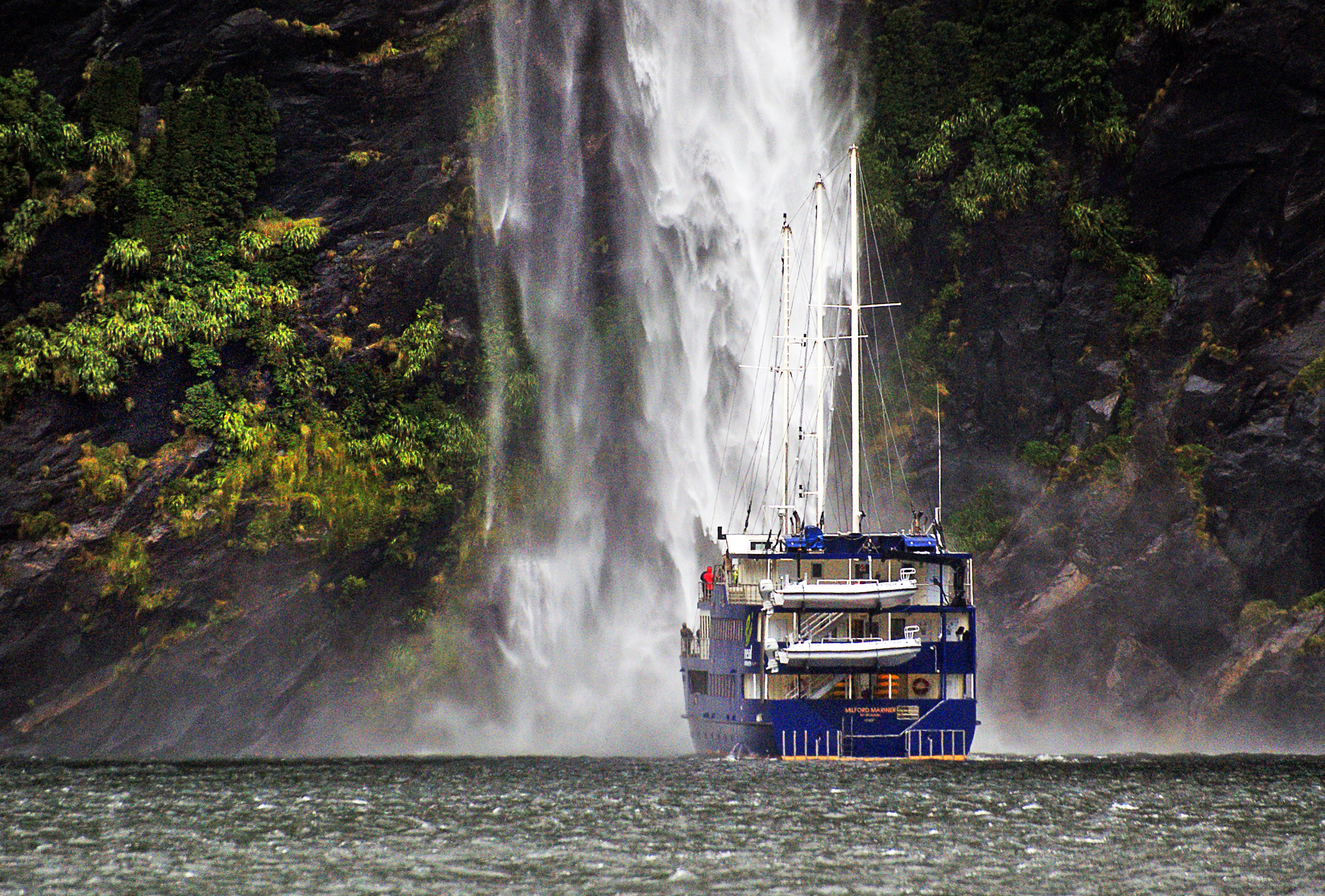 A cruise boat passing beneath Stirling Falls in Milford Sound