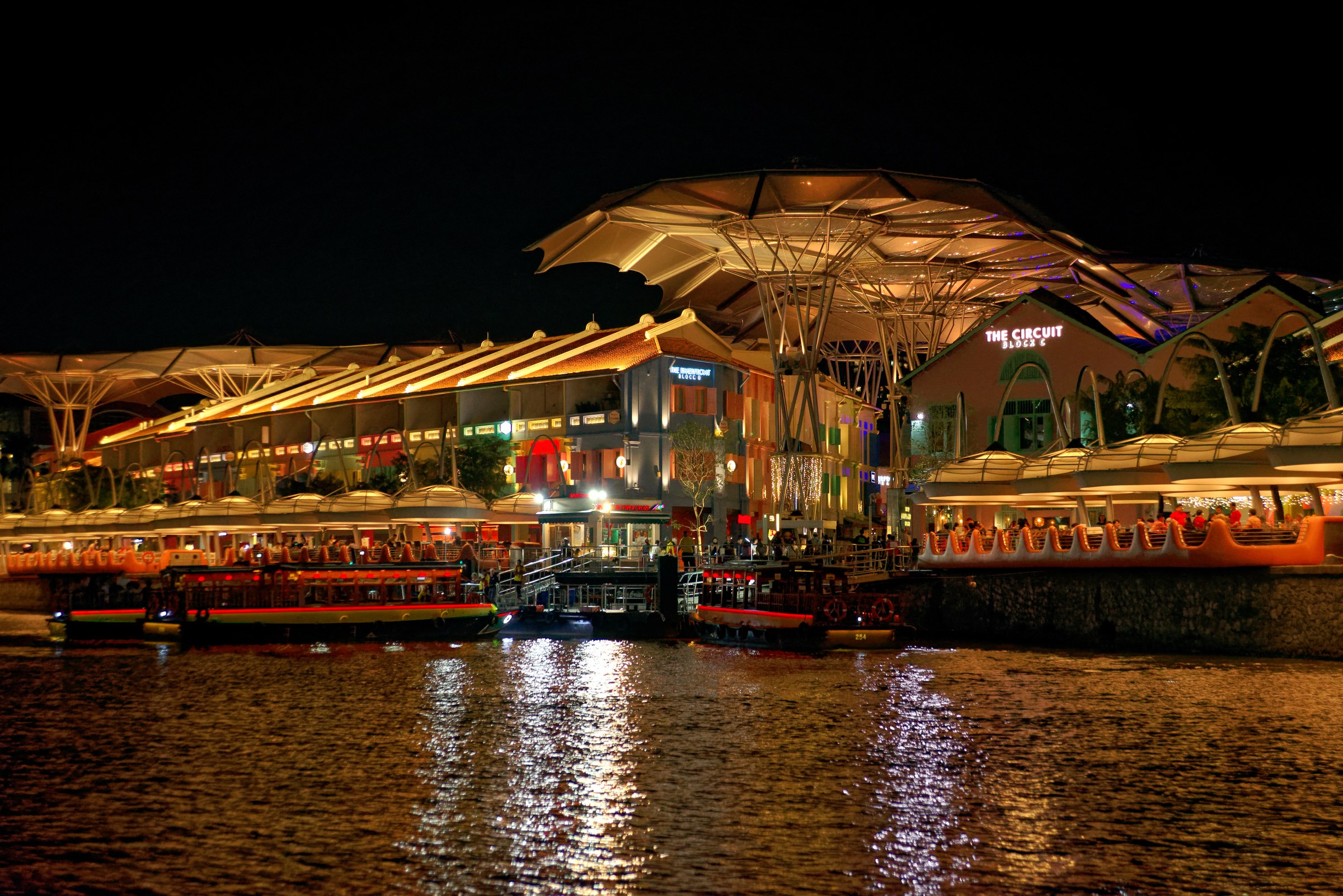 Clarke Quay Singapore riverside at night with illuminated canopy and river boats