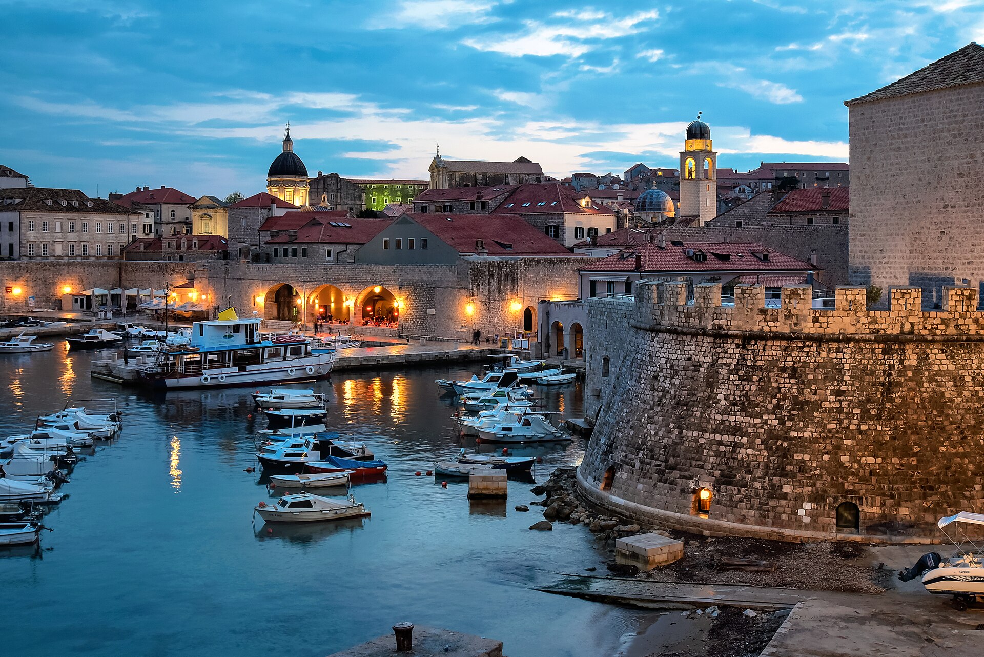 Dubrovnik's Old Harbour at dusk with boats moored beneath the lit city walls