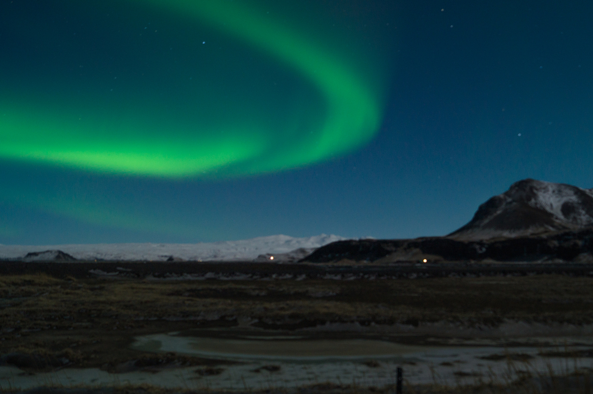 Bright green aurora arc over snowy Icelandic mountains